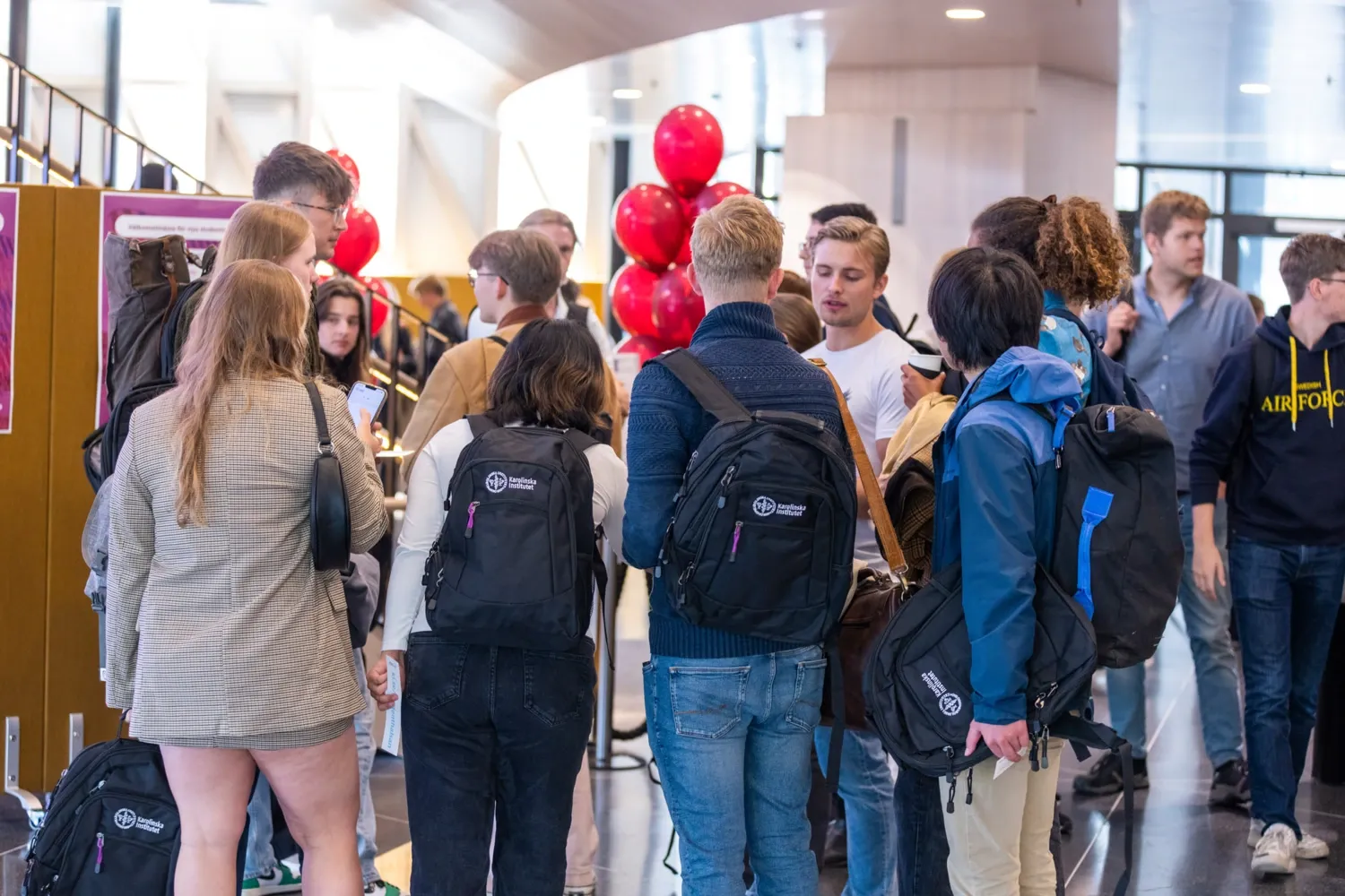Studenter i grupp minglar på välkomstmässa med sina KI-ryggsäckar. Ballonger syns i bakgrunden.
