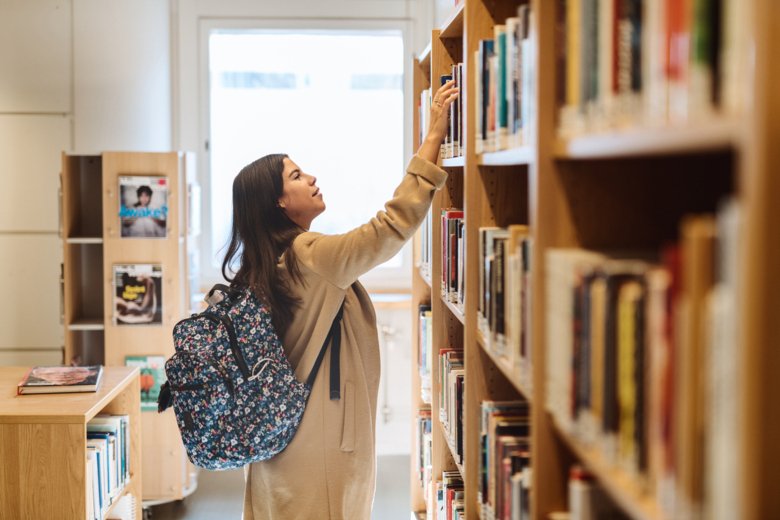 Student tar bok från hylla i biblioteket.