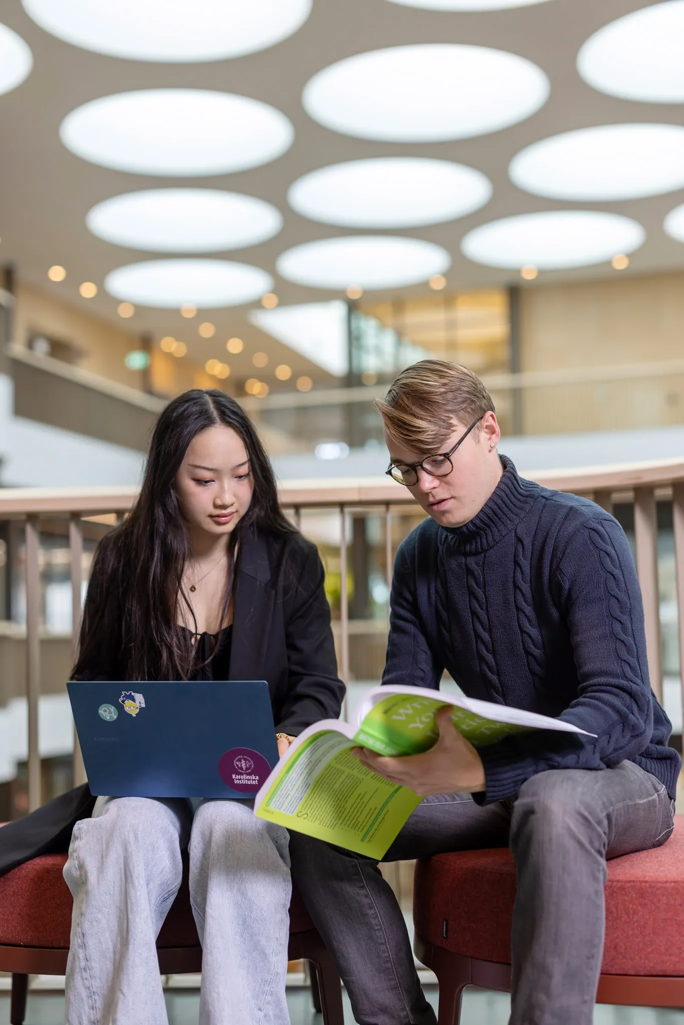 En kvinnlig och en manlig student som tittar ner i dator och bok