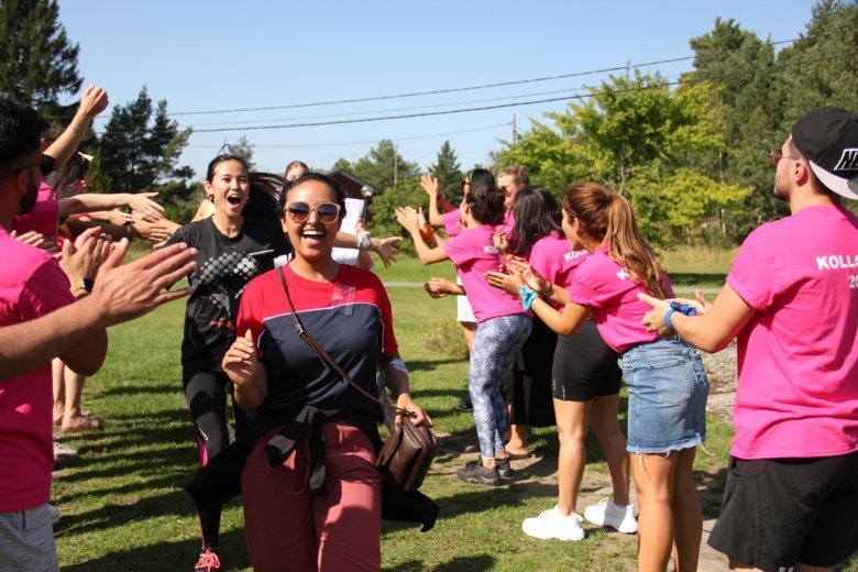 En grupp glada studenter på en gräsmatta med rosa t-shirts där det står kollo.