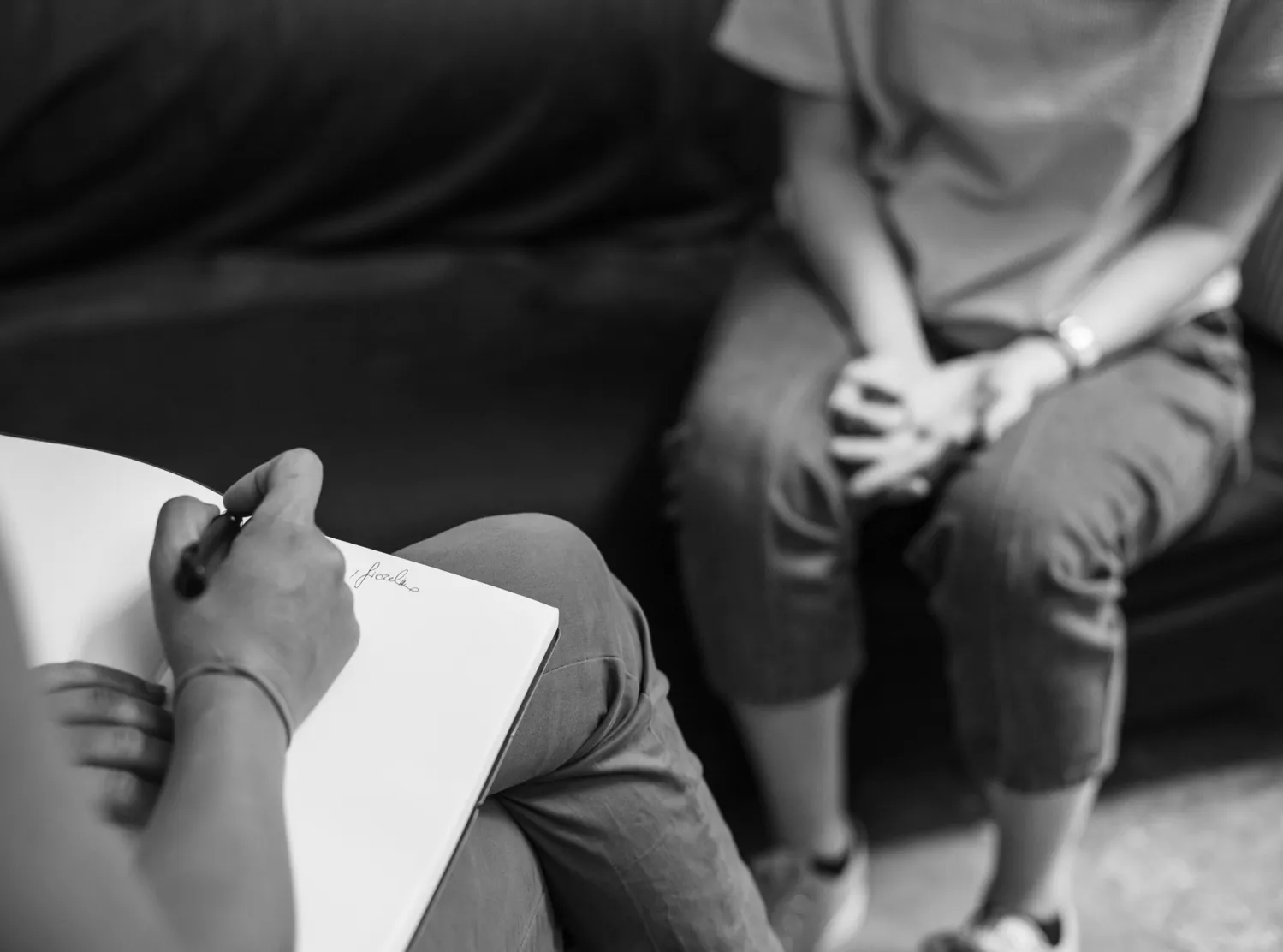 Två personer sitter i soffor och pratar med varandra. En av de skriver i ett block.