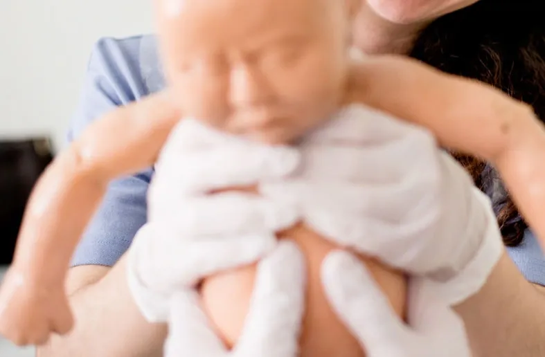 En barnmorskestudent håller upp en bebisdocka på utbildningen för barnmorskor på KI.