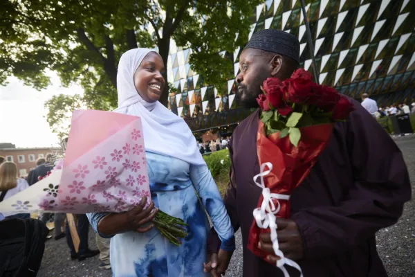 En examensstudent håller i en blombukett och tittar glatt på sin pappa.