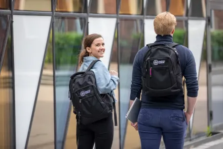 Två studenter utanför Aula Medica med KI ryggsäckar. Den ena vänder sig om och tittar leende mot kameran.