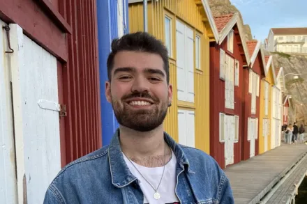 Porträtt av student som står leende framför färgglada hus.