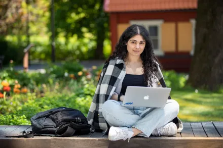 Studenter utomhus på campus Solna en solig vårdag 2022. || Student som sitter utomhus på campus Solna med laptop