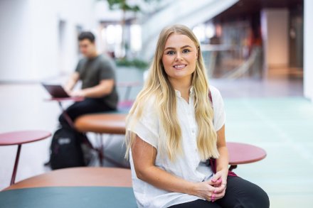 Kvinnlig student som sitter ner och tittar in i kameran