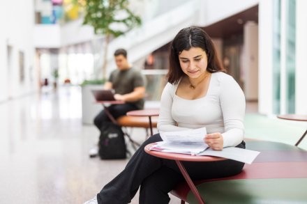 Kvinnlig student som sitter ner och läser i bok